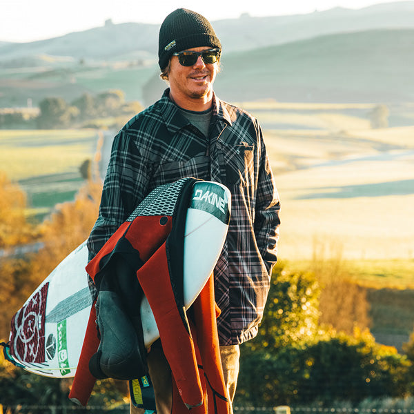 Surfer Albee Layer holding surfboard and wetsuit 